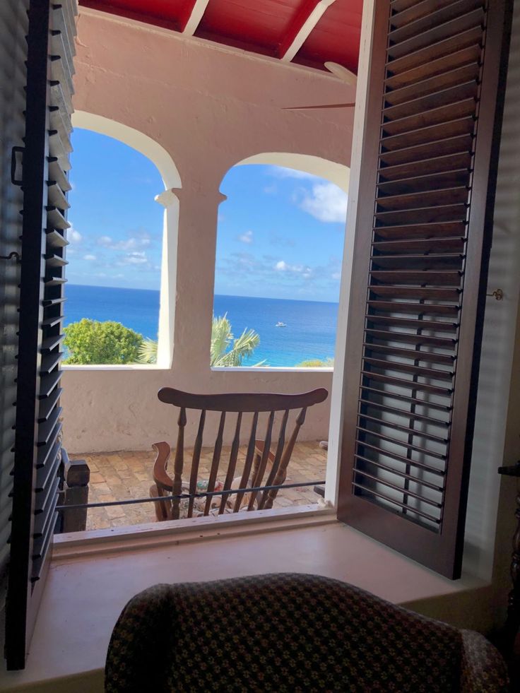 a rocking chair sitting on top of a balcony next to an open window overlooking the ocean