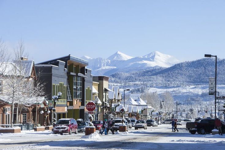 people are walking down the street in front of some buildings with mountains in the background