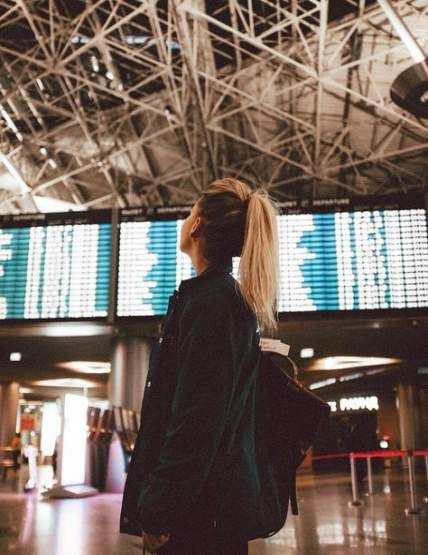 a woman standing in an airport with her back to the camera, looking up at some electronic screens