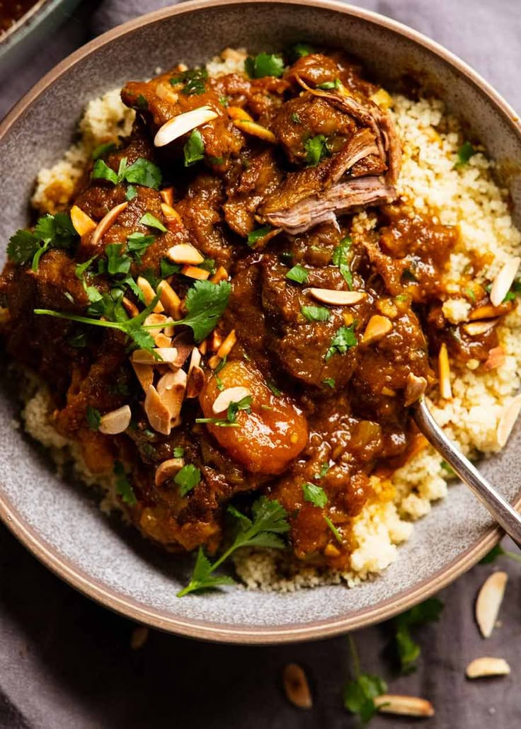 a bowl filled with rice and meat covered in gravy, garnished with parsley