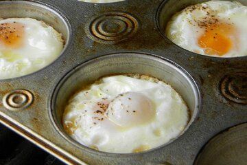 three eggs in a muffin tin on top of an oven burner with other food items