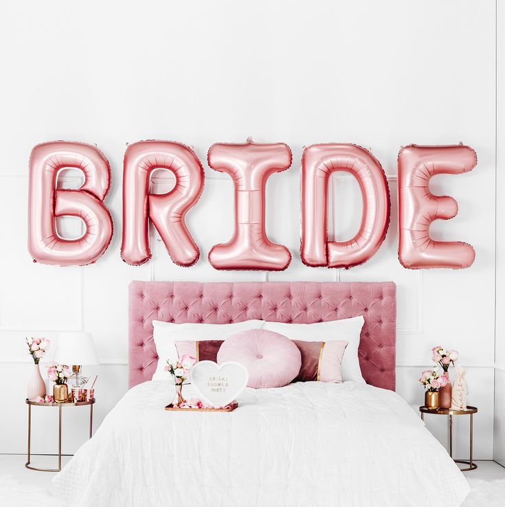 a bed with pink pillows and balloons on the headboard that read bride in large letters above it