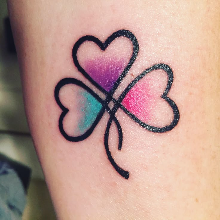 a four - leaf clover tattoo on the left thigh with pink, blue and green colors