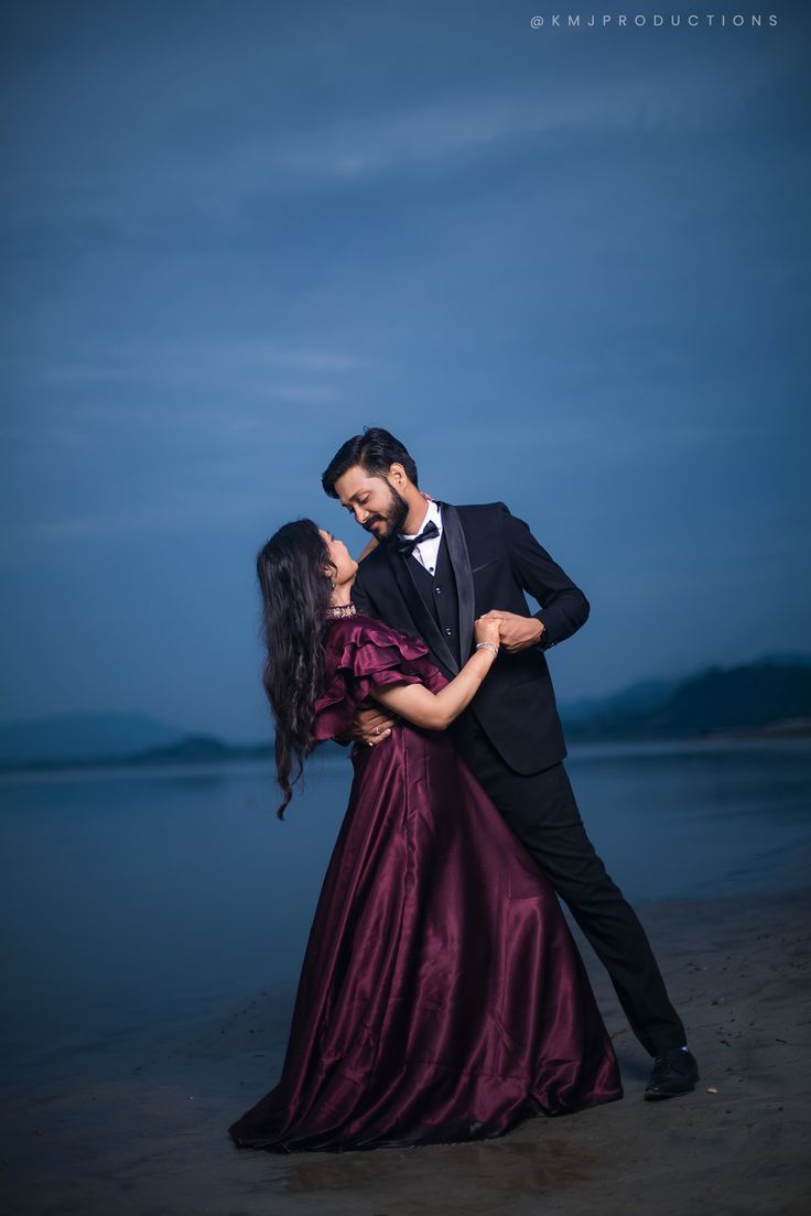 a man in a tuxedo hugging a woman on the beach