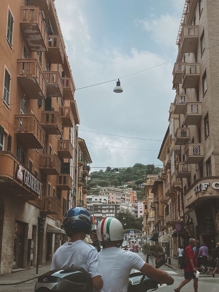 two people riding on the back of a motorcycle down a street next to tall buildings