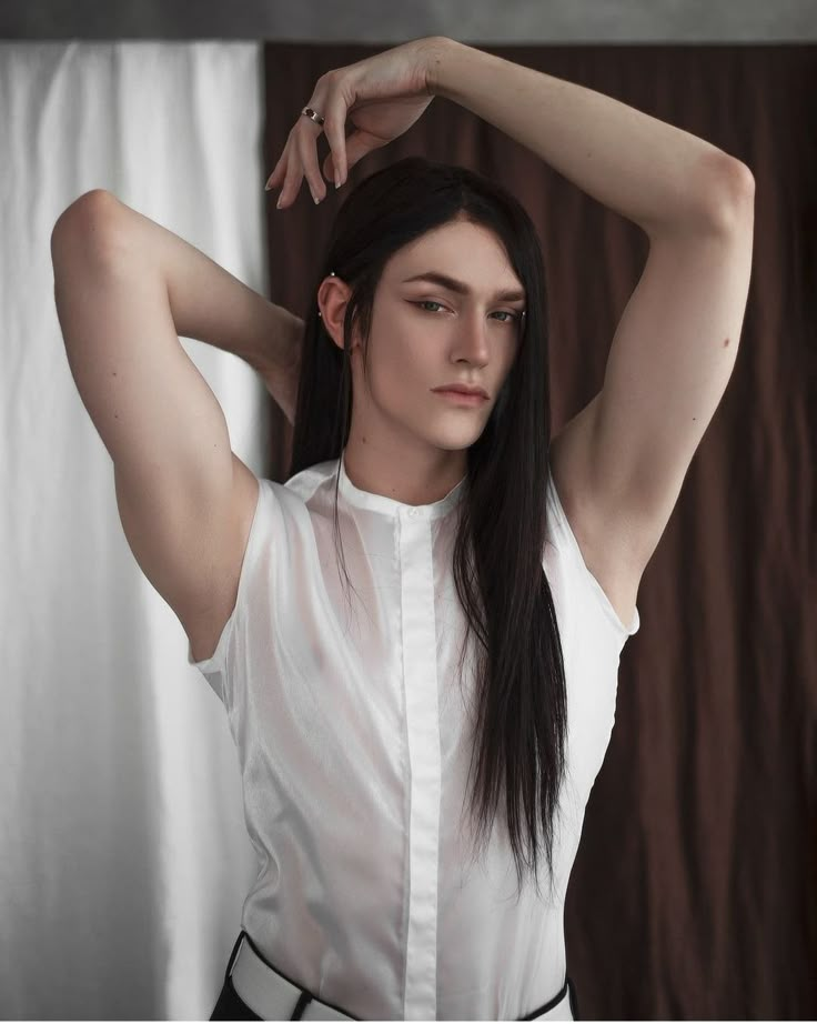 a woman with long black hair wearing a white shirt and black pants is posing for the camera