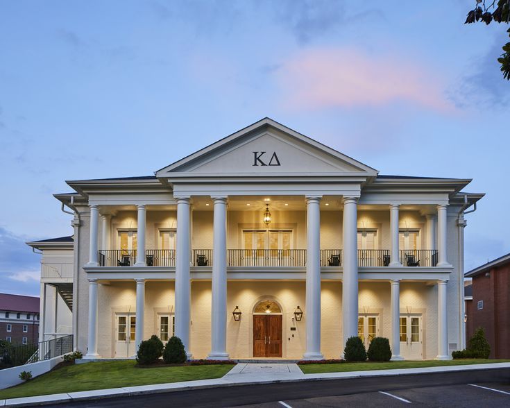 a large white building with columns on the front and side sides at dusk, lit up by street lights