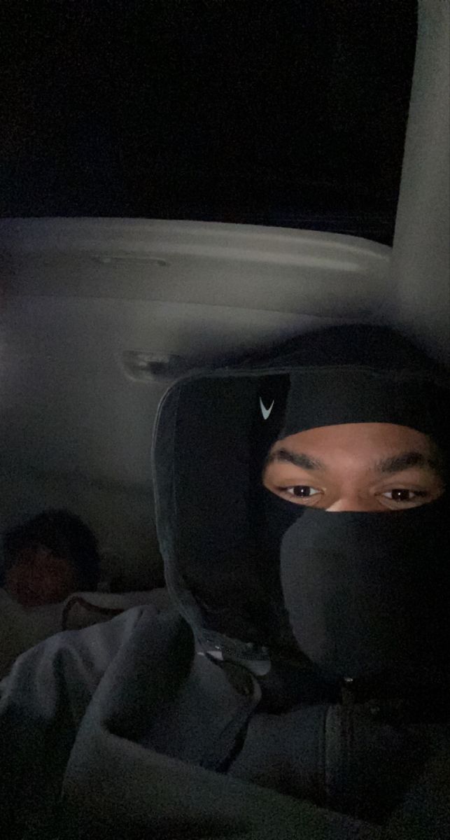 a man wearing a black hoodie sitting in the back of a car at night