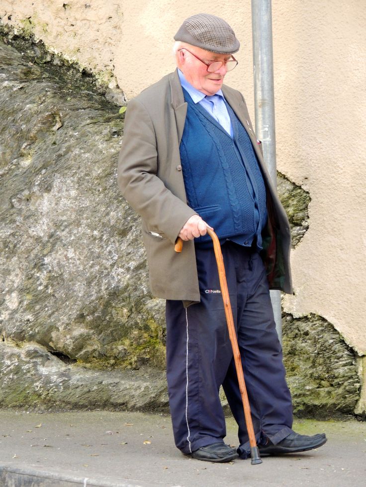 an old man is standing on the sidewalk with his cane in hand and looking down