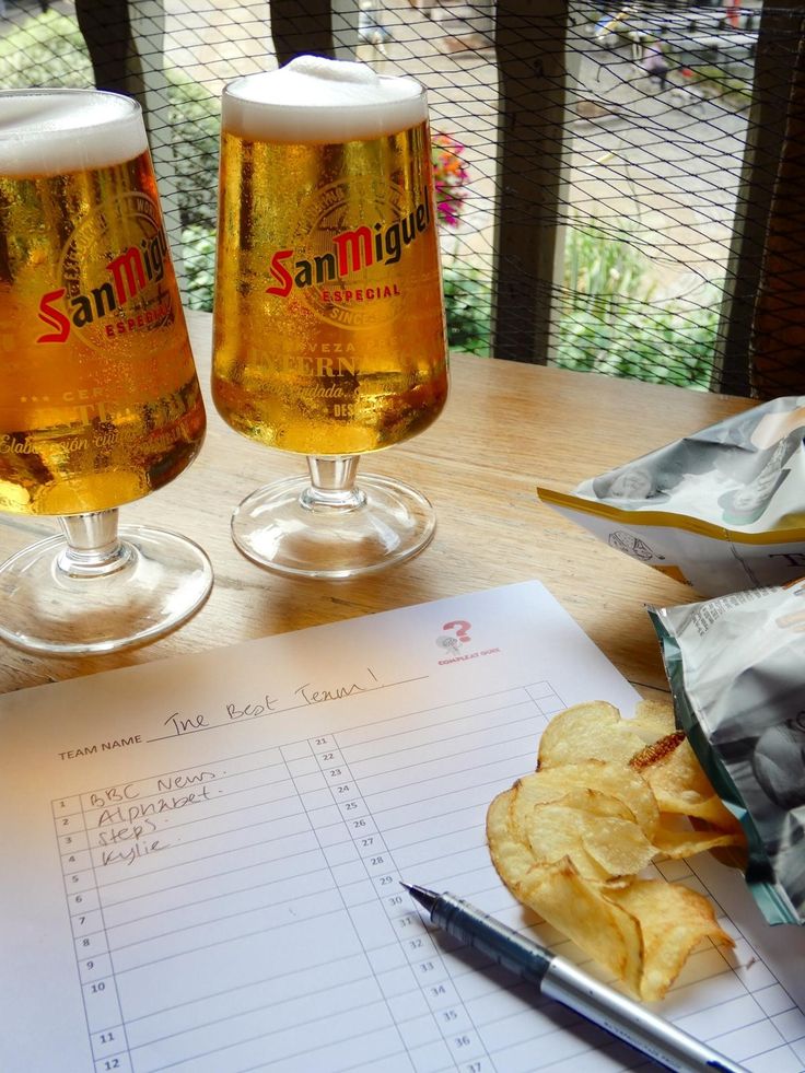 two glasses of beer sitting on top of a table next to chips and a pen