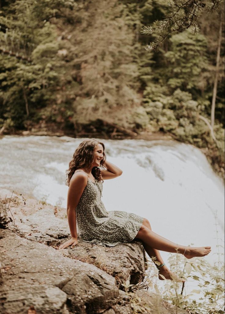 a woman sitting on top of a rock next to a river