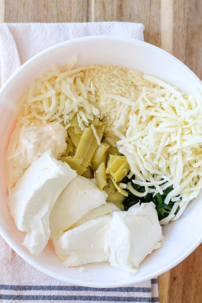 a white bowl filled with cheese and other food on top of a wooden table next to a napkin