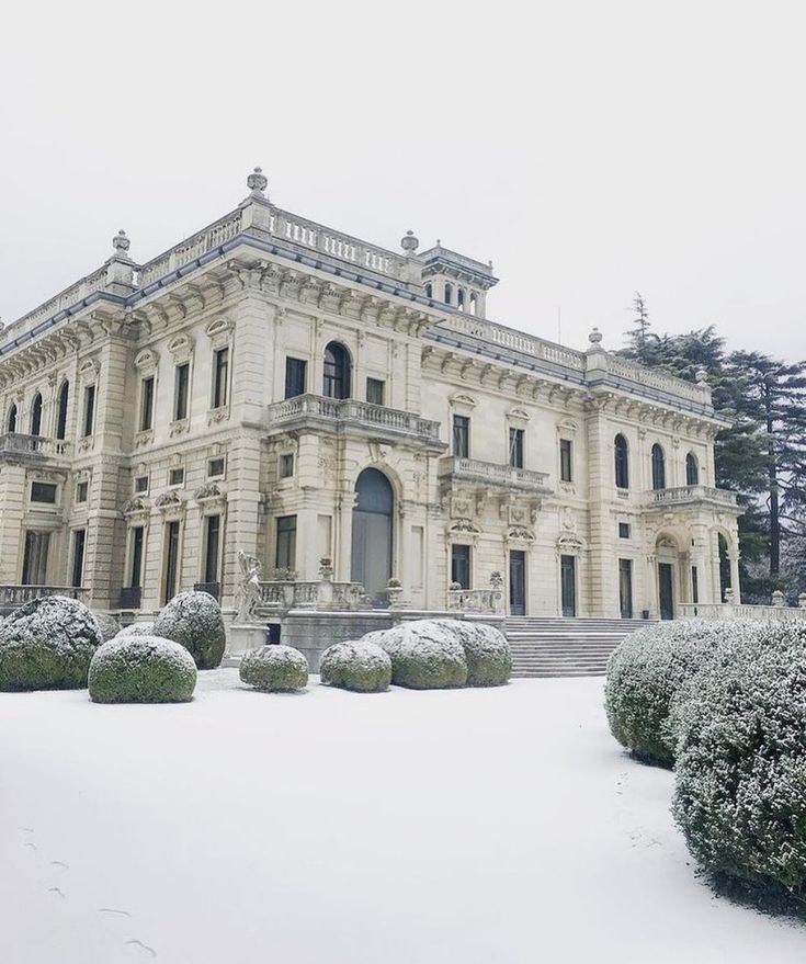 a large white building sitting in the middle of a snow covered field with trees and bushes