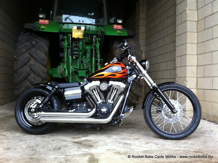 an orange and black motorcycle parked in front of a green tractor on the side of a building