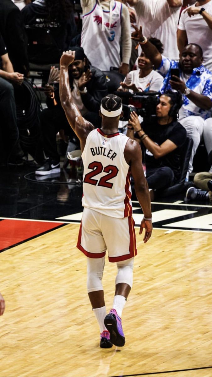 a basketball player is walking on the court with his arms in the air as people look on