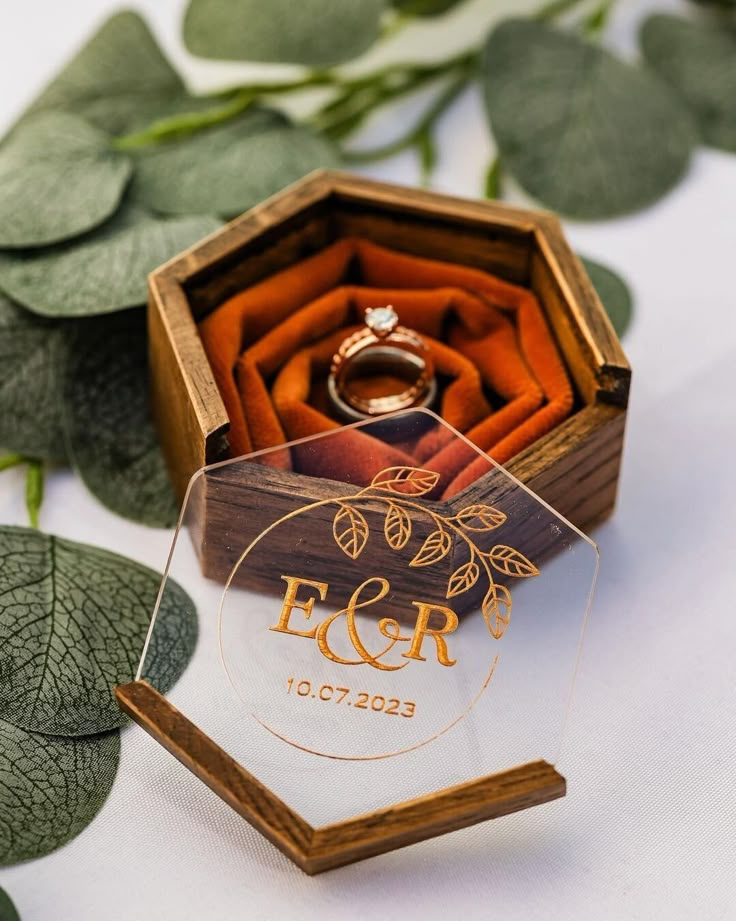 a wedding ring sits in a wooden box on top of some leaves and greenery