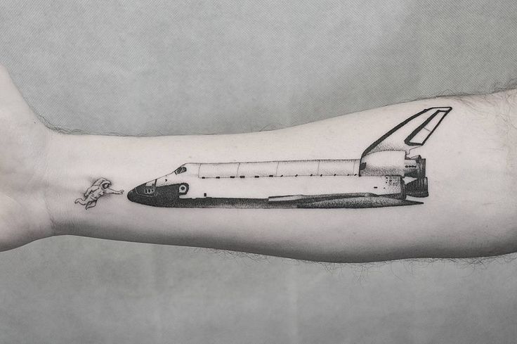 a black and white photo of a space shuttle tattoo on the left arm, with an astronaut's rocket attached to it