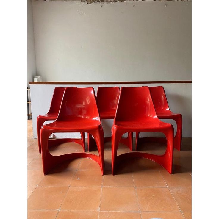 three red chairs sitting next to each other on a tile floor in front of a wall