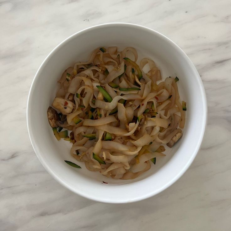 a white bowl filled with noodles sitting on top of a table next to a marble counter