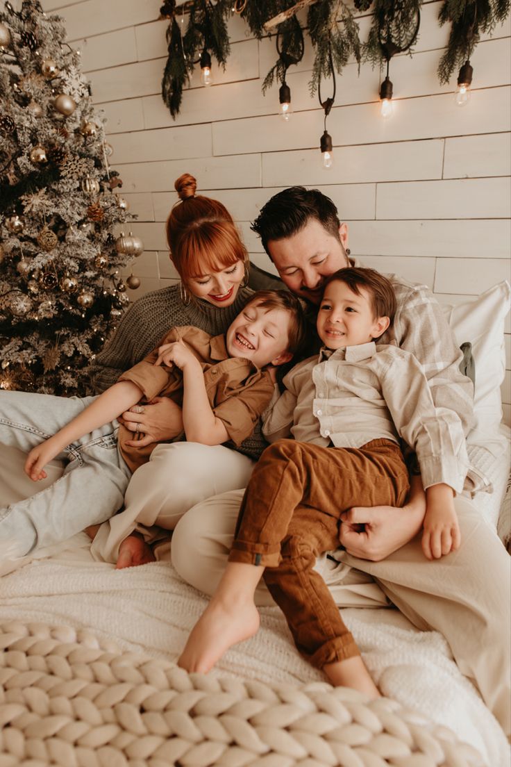 a family laying in bed with christmas tree and lights on the wall behind them, all smiling