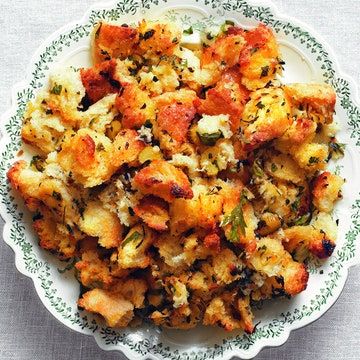 a white bowl filled with stuffing on top of a table next to a knife and fork