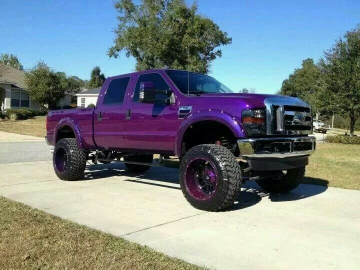 the purple truck is parked on the sidewalk in front of some trees and grass,