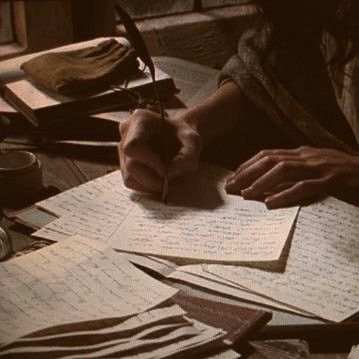 a person sitting at a table with lots of papers and writing utensils on it