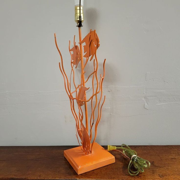 an orange lamp is sitting on a table next to a branch with leaves in it