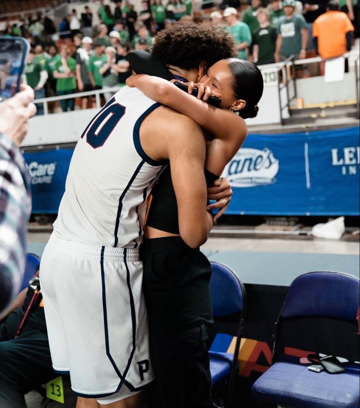 two women hugging each other in the middle of a basketball court while people watch from the stands