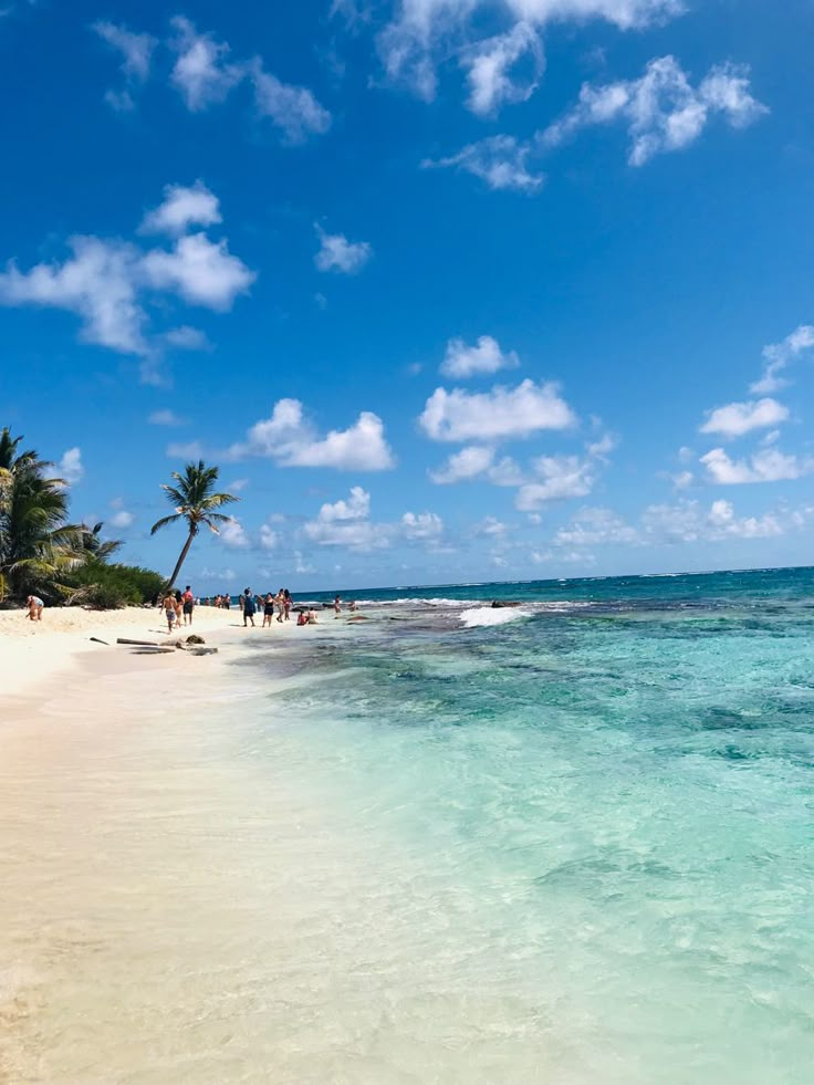 people are walking along the beach on a sunny day with blue skies and white clouds