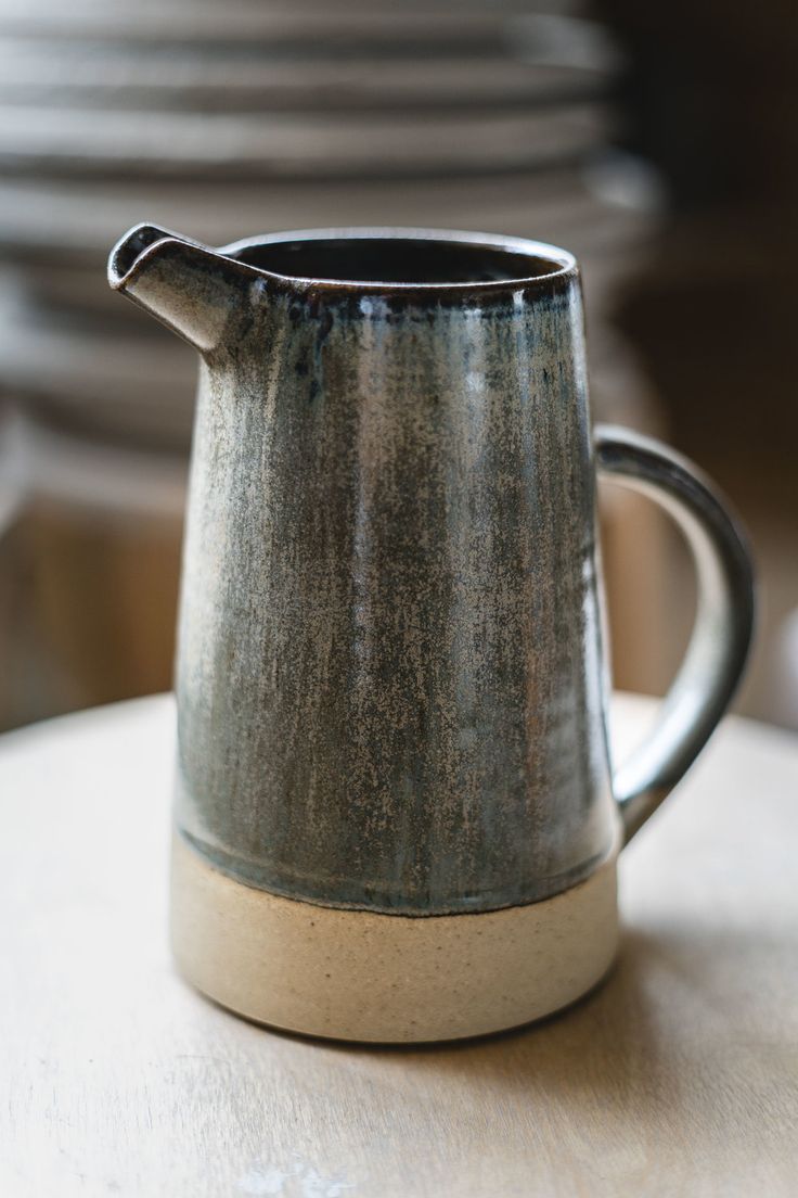 a gray pitcher sitting on top of a table next to stacks of plates and bowls