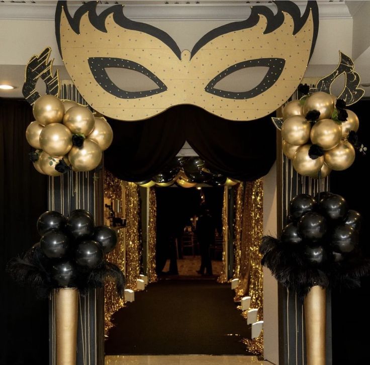 an entrance decorated with black and gold balloons, masquerade masks and streamers