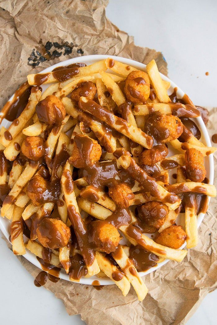 a white bowl filled with french fries covered in gravy on top of brown paper