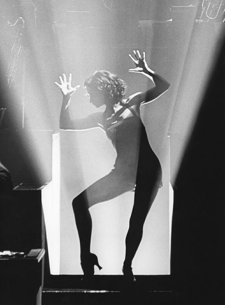 a black and white photo of a woman on stage with her hands in the air