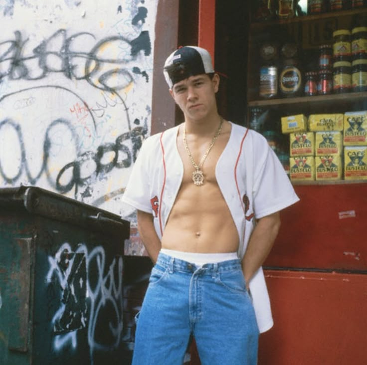 a shirtless man leaning against a wall with graffiti on it's walls behind him