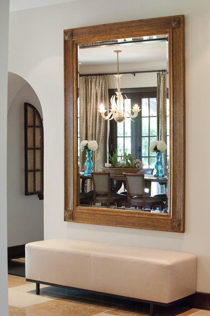 a large mirror hanging on the wall above a bench in front of a dining room table