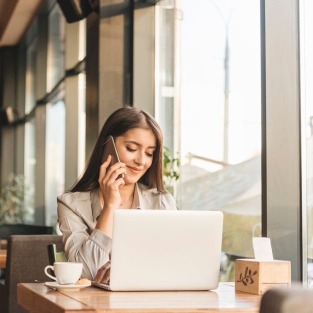 a woman sitting at a table talking on her cell phone while using a laptop computer