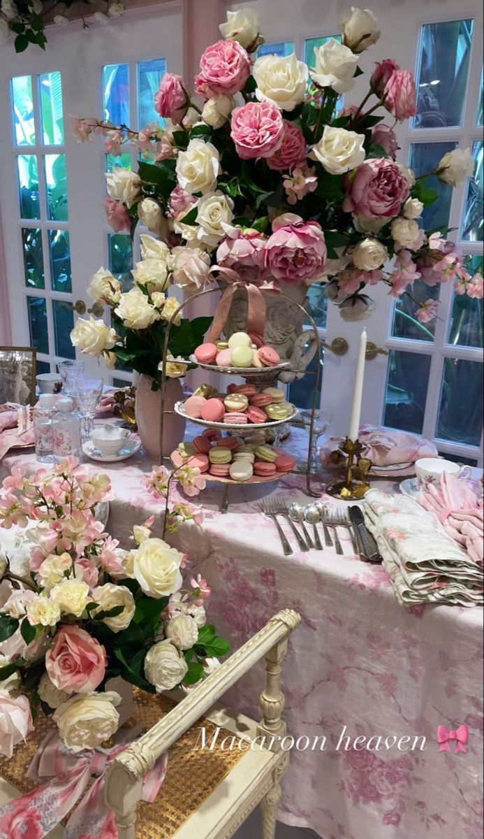 a table topped with lots of pink and white flowers next to a tall vase filled with cupcakes