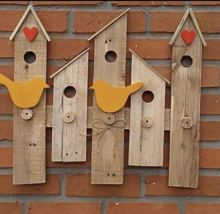 three wooden birdhouses with yellow birds and red hearts hanging on the side of a brick wall