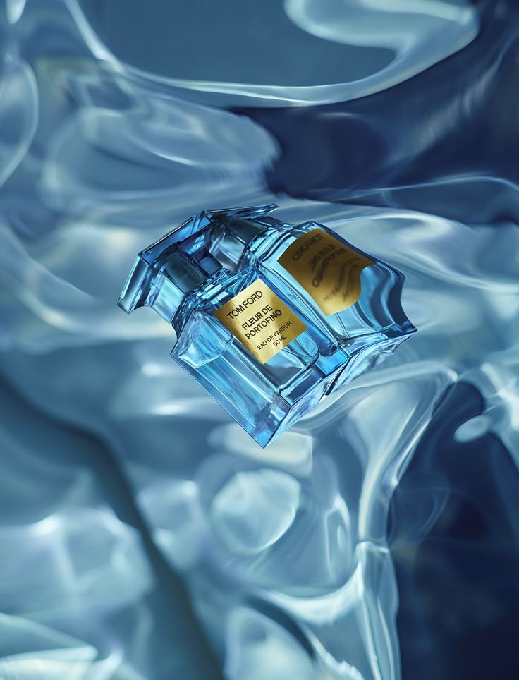 a bottle of perfume sitting on top of a blue liquid filled surface with water swirling around it