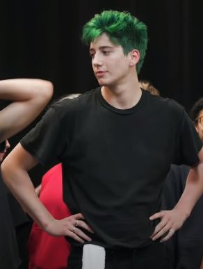 a young man with green hair standing in front of other people wearing black shirts and red pants