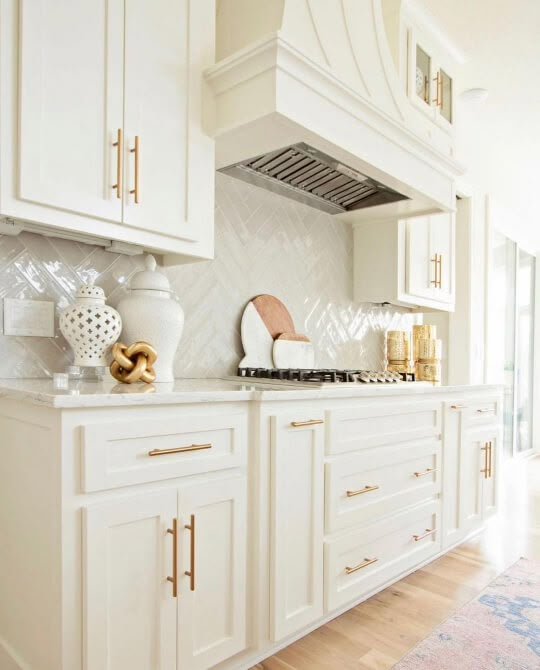 a kitchen with white cabinets and gold trim on the counter tops, along with an oven hood