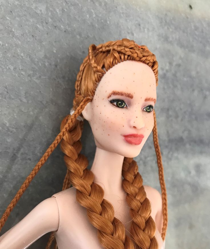 a doll with long red hair and braids on it's head is posed next to a gray wall