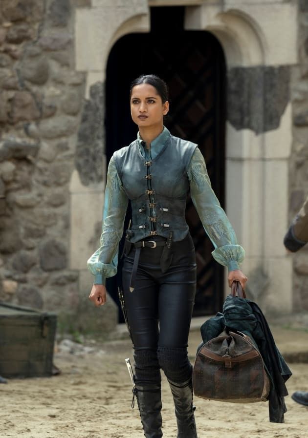 a woman walking down a dirt road carrying a bag and wearing black pants with laces