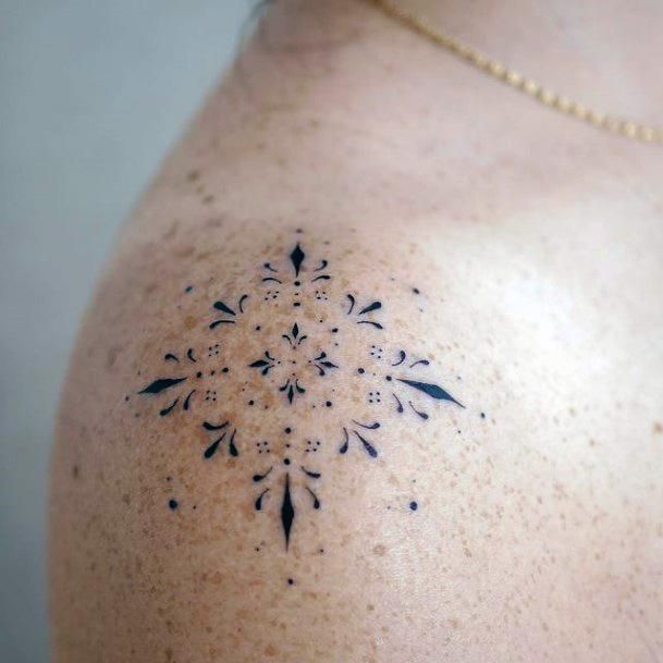 the back of a woman's shoulder with an intricate tattoo design on her left shoulder