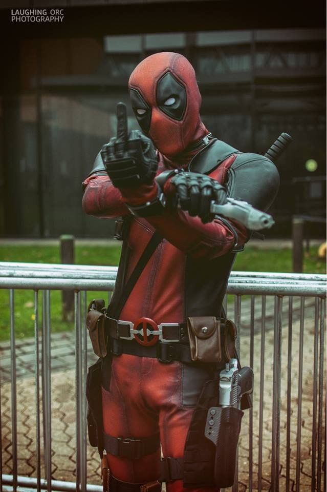 a man dressed as deadpool pointing at something in his hand while standing next to a fence