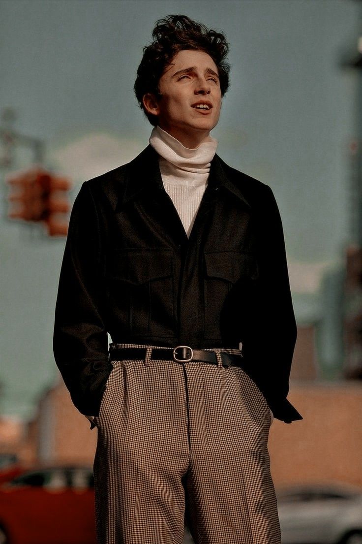 a man standing in front of a building wearing a black shirt and brown plaid pants