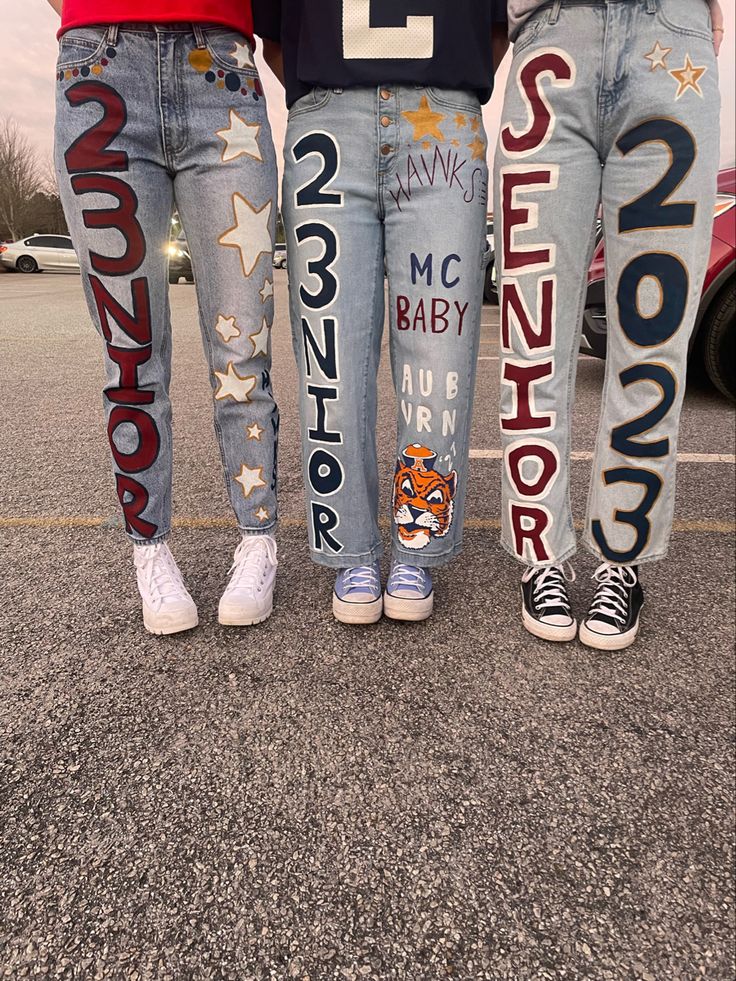 three people standing in the middle of a parking lot wearing jeans with letters painted on them