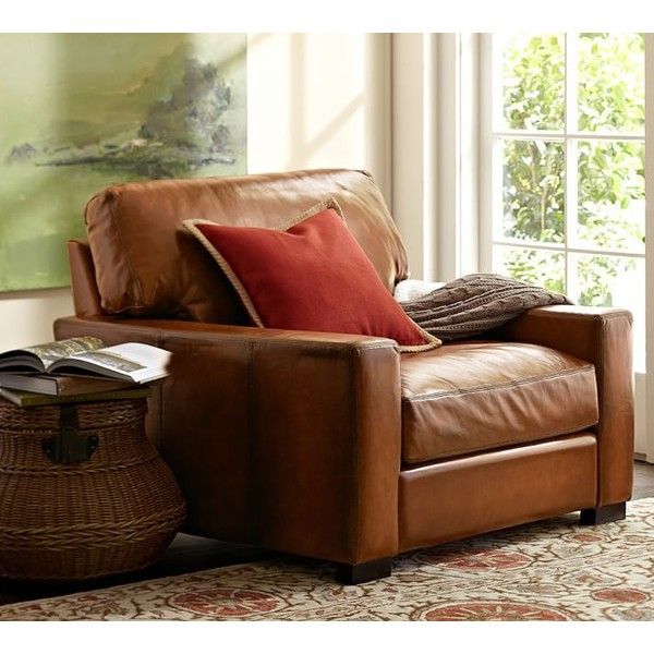 a brown leather chair sitting in front of a window next to a basket filled with books