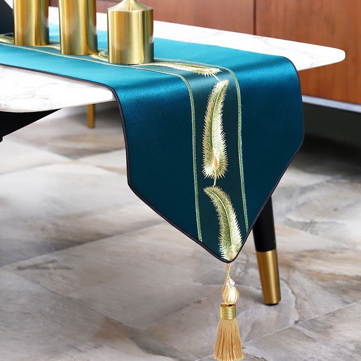 a blue table runner with gold accents and tassels on the edge is sitting on a marble floor